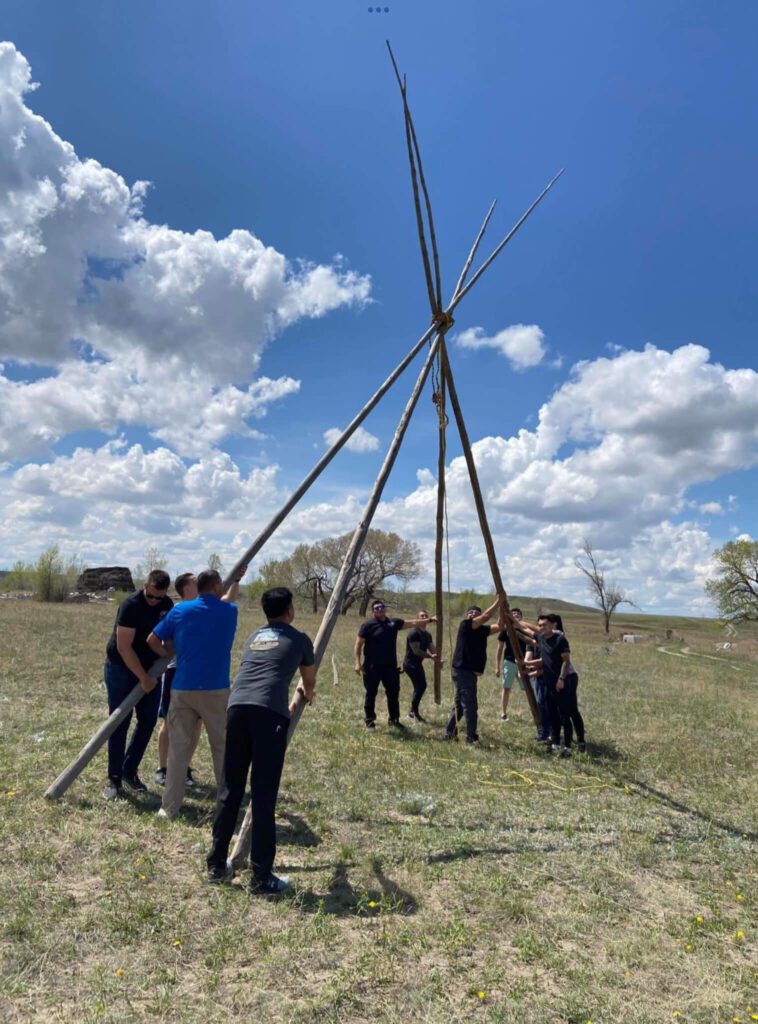 A group of people standing around a teepee.